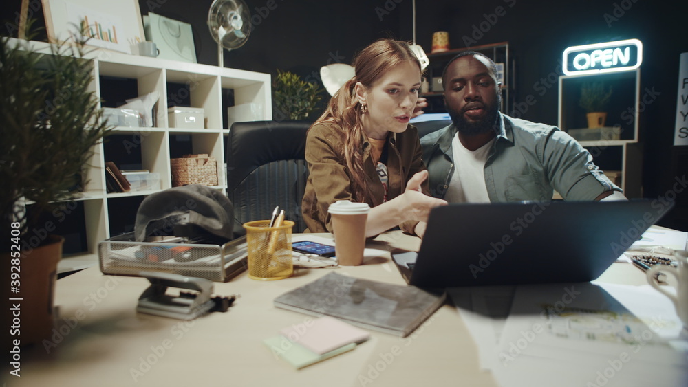 African american man hugging surprised woman near laptop in dark office. African american man hugging surprised woman near laptop in dark office.