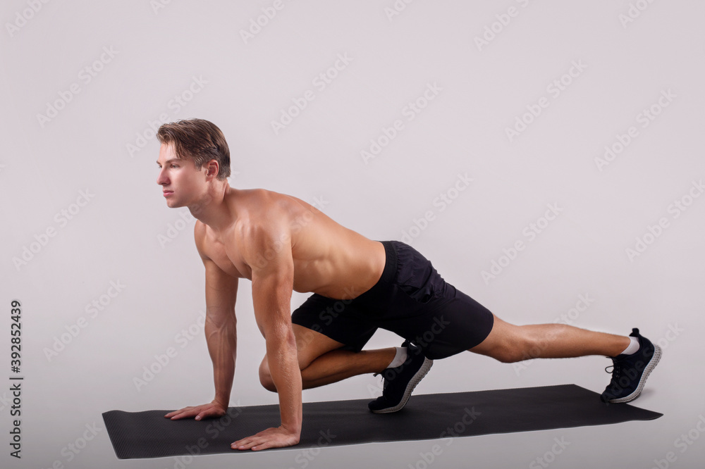 Obraz premium Healthy lifestyle and sports. Strong young man with naked chest exercising on yoga mat over light studio background