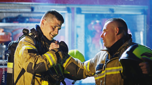 Portrait of two young firefighters on the rain in front of fire engine in full uniform. Fire dril. High quality photo