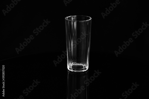 Closeup of an empty glass of water on a black background. Empty glass of water on a black glossy surface.