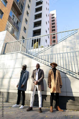 Stylish African- American men posing against a brick wall background with sun shadow
