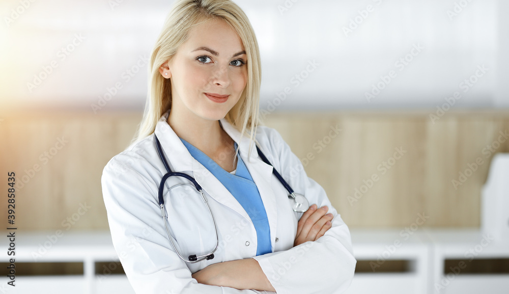 Woman-doctor at work while standing straight in sunny clinic. Blonde cheerful physician ready to help patients Woman-doctor at work while standing straight in sunny clinic. Blonde cheerful physician ready to help patients