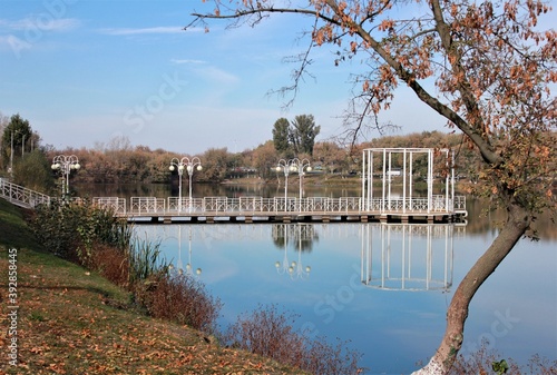 Autumn trees and pier are reflected in the city pond on a Sunny day