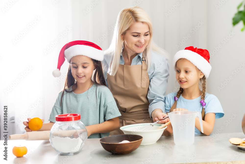 Happy family in the kitchen. Mother and two little daughters preparing the dough for Christmas cookies. Happy family in the kitchen. Mother and two little daughters preparing the dough for Christmas cookies.