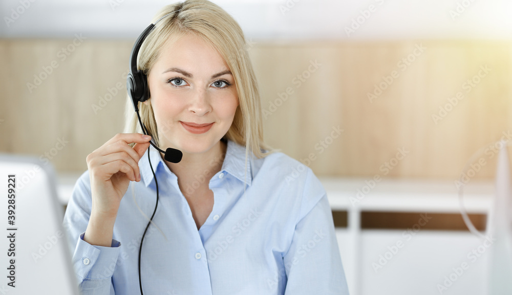 Blonde business woman sitting and communicated by headset in call center in sunny office. Concept of telesales business Blonde business woman sitting and communicated by headset in call center in sunny office. Concept of telesales business