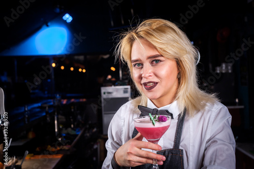 Confident girl bartender mixes a cocktail while standing near the bar counter in pub photo