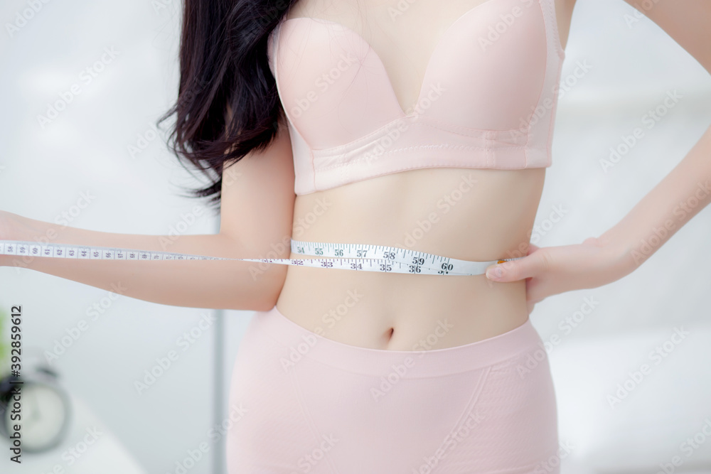 Beautiful young asian woman sexy body slim measuring abdomen for control weight loss in the room, beauty girl belly thin have cellulite with tape measure for diet, health and wellness concept. - obrazy, fototapety, plakaty 