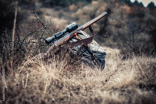 Quadro su tela Hunting rifle with a scope near a backpack on a background of an autumn forest,
