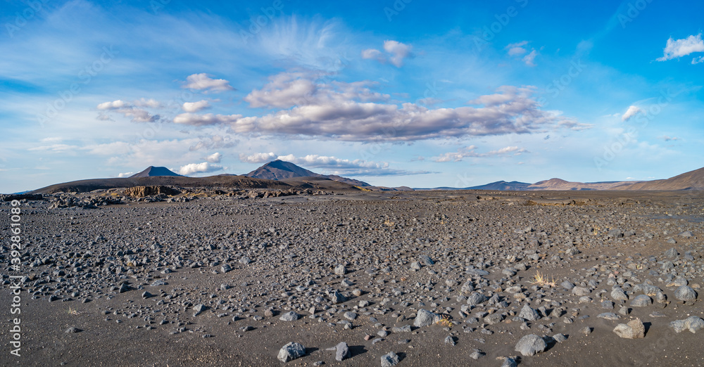 Panoramic view over Icelandic landscape of the deadliest volcanic desert in Highlands, with stones and rocks thrown by volcanic eruptions and hiking trek along the off road, Iceland, summer, blue sky.