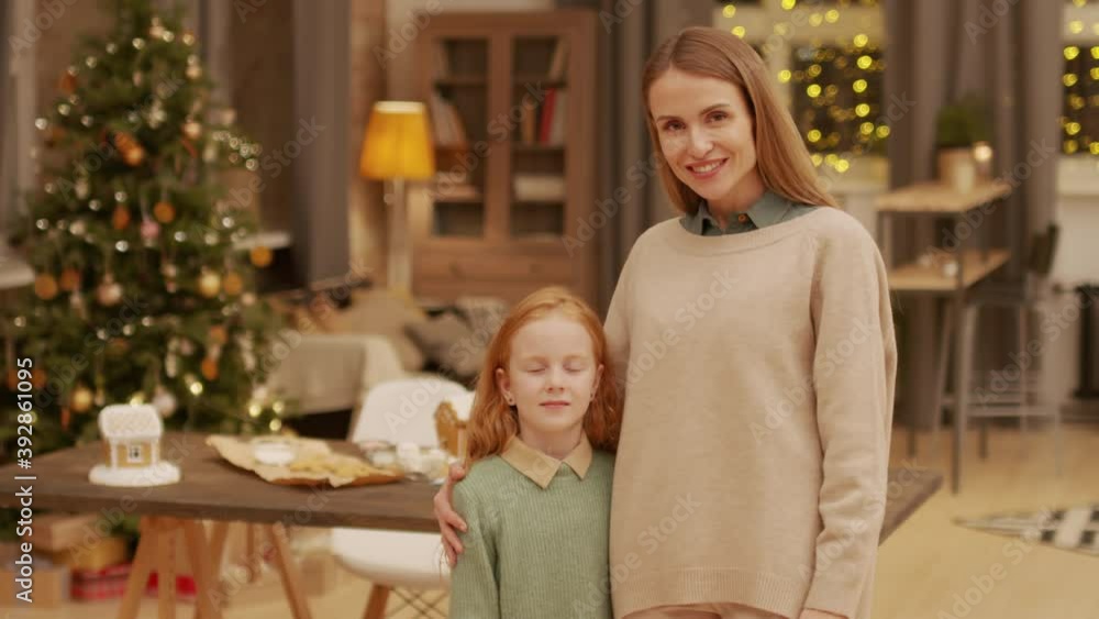 Medium portrait of beautiful caucasian woman and her daughter standing in living room decorated for christmas looking at camera smiling Medium portrait of beautiful caucasian woman and her daughter standing in living room decorated for christmas looking at camera smiling