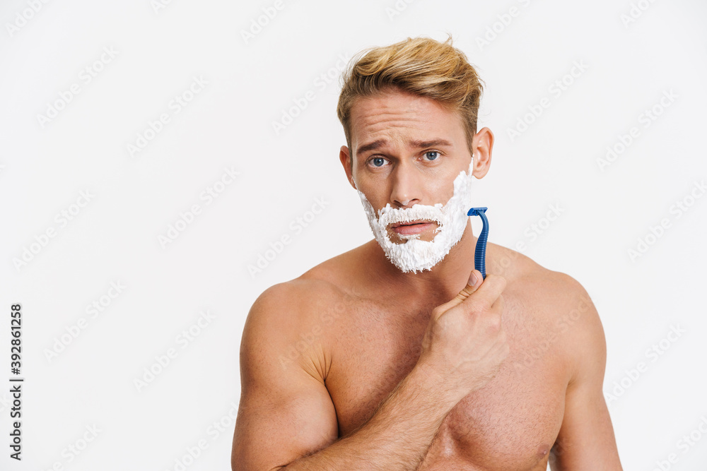 Unhappy caucasian shirtless man shaving with foam and razor