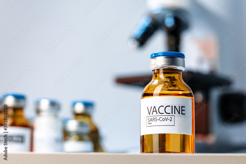 Vial of Covid-19 vaccine next to a microscope Vial of Covid-19 vaccine next to a microscope