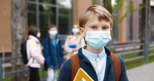 Close up portrait of Caucasian happy schoolboy standing outdoors with copybooks and putting off medical mask. Male student in mask near school after lessons smiling to camera. Quarantine concept © VAKSMANV
