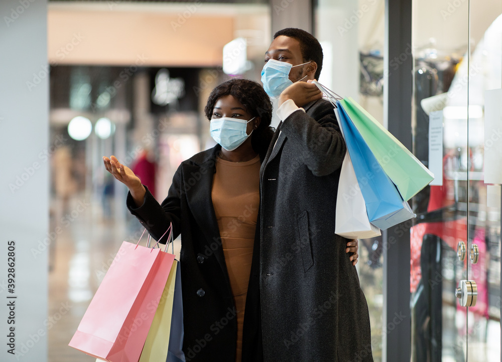 Happy african american family in coats and protective masks walking in mall after buying clothes at Black Friday