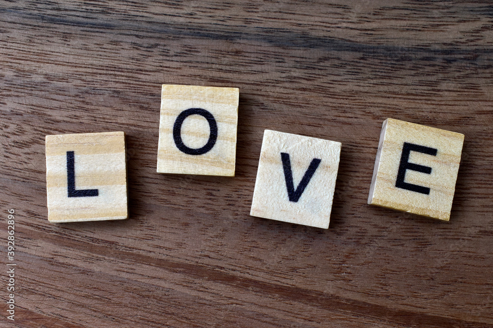 LOVE spelt as a word using wooden scrabble type letters on a wooden background.