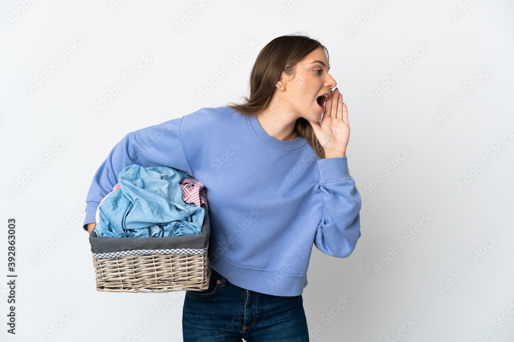 Young Lithuanian woman holding a clothes basket isolated on white background shouting with mouth wide open to the side Young Lithuanian woman holding a clothes basket isolated on white background shouting with mouth wide open to the side