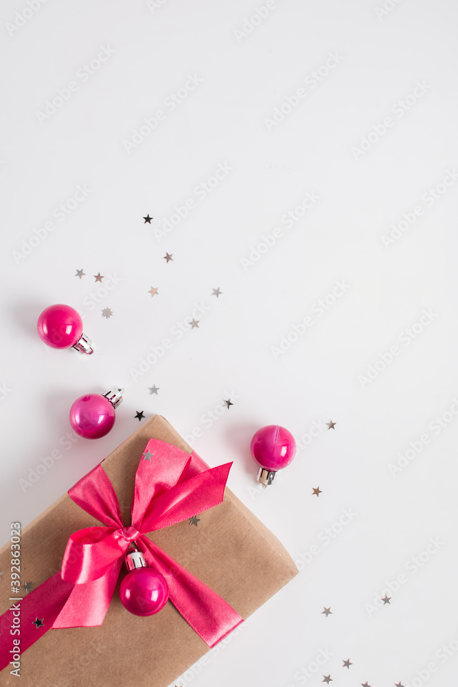 Christmas composition with craft paper gift with pink ribbon bow, confetti and pink balls on white background. Copy space