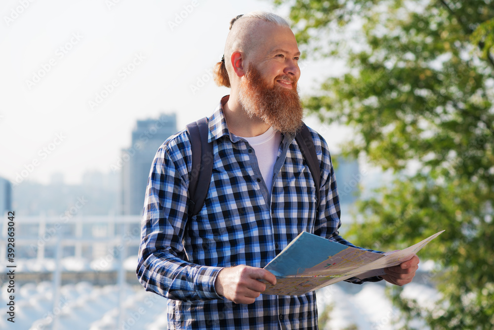 Smiling caucasian hipster bearded man satisfied with active vacation having trip. Smiling male traveler walking with map having city tour on autumn weekends. Travel concept.