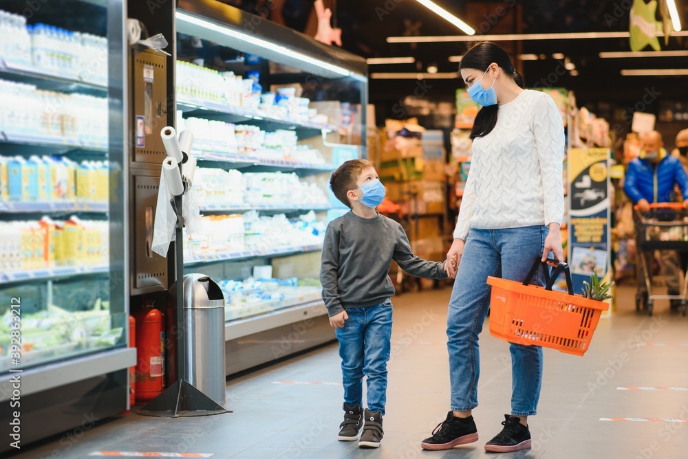 Shopping with kid during virus outbreak. Mother and child wearing surgical face mask buying fruit in supermarket. Mom and little boy buy fresh vegetable in grocery store. Family in shop.