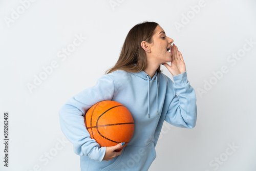 Young Lithuanian woman playing basketball isolated on white background shouting with mouth wide open to the side © luismolinero