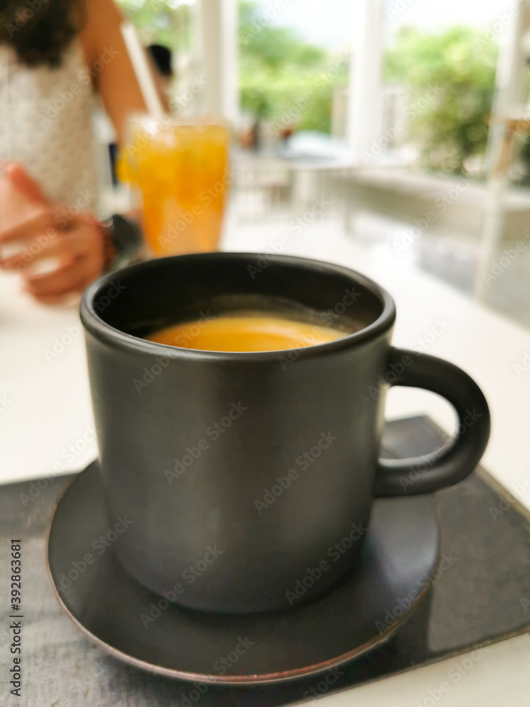 black coffee mug on white table in coffee shop atmosphere and blur photo of women sit on the other side 