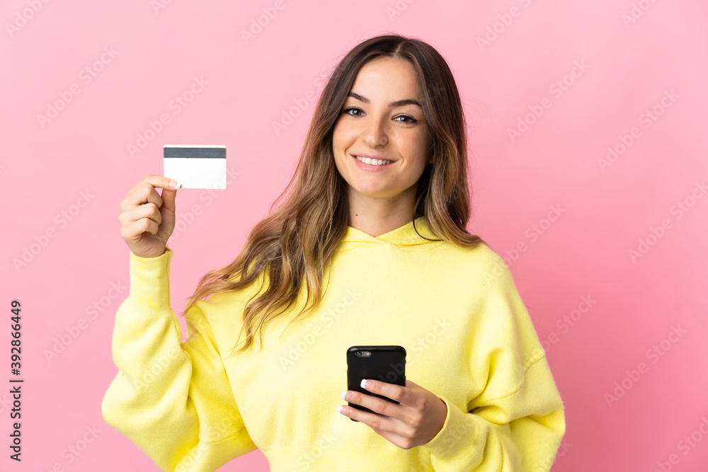 Young Romanian woman isolated on pink background buying with the mobile with a credit card Young Romanian woman isolated on pink background buying with the mobile with a credit card