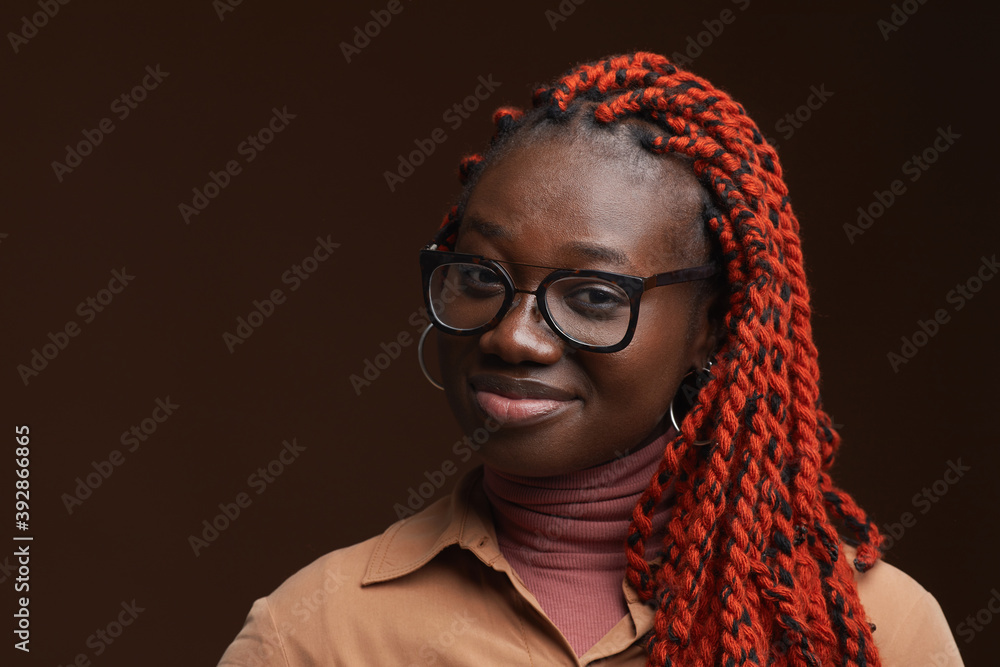 Close up portrait of confident African-American woman with braided hair smiling at camera while posing against dark brown background in studio, copy space Close up portrait of confident African-American woman with braided hair smiling at camera while posing against dark brown background in studio, copy space