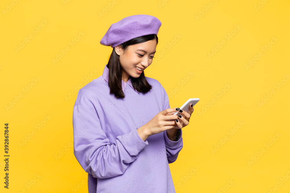 happy asian woman in beret looking at smartphone isolated on yellow happy asian woman in beret looking at smartphone isolated on yellow