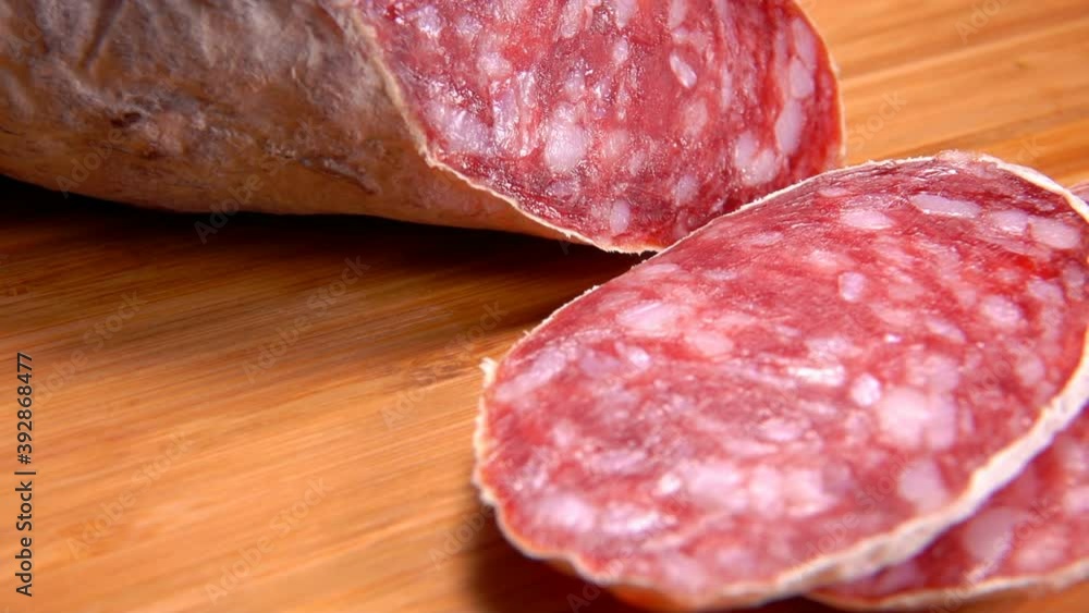 Close-up of delicious dry sausage in white skin cut into slices with a thin knife on a wooden board Close-up of delicious dry sausage in white skin cut into slices with a thin knife on a wooden board