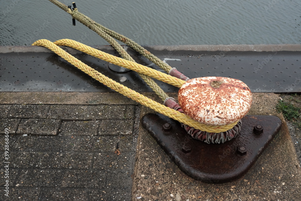 Φωτογραφία Rostiger Poller mit Schiffstau in Gelb bei Regenwetter im Hafen von Norddeich an