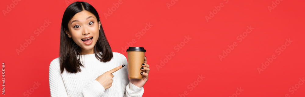 excited asian woman pointing with finger at disposable cup isolated on red, banner excited asian woman pointing with finger at disposable cup isolated on red, banner