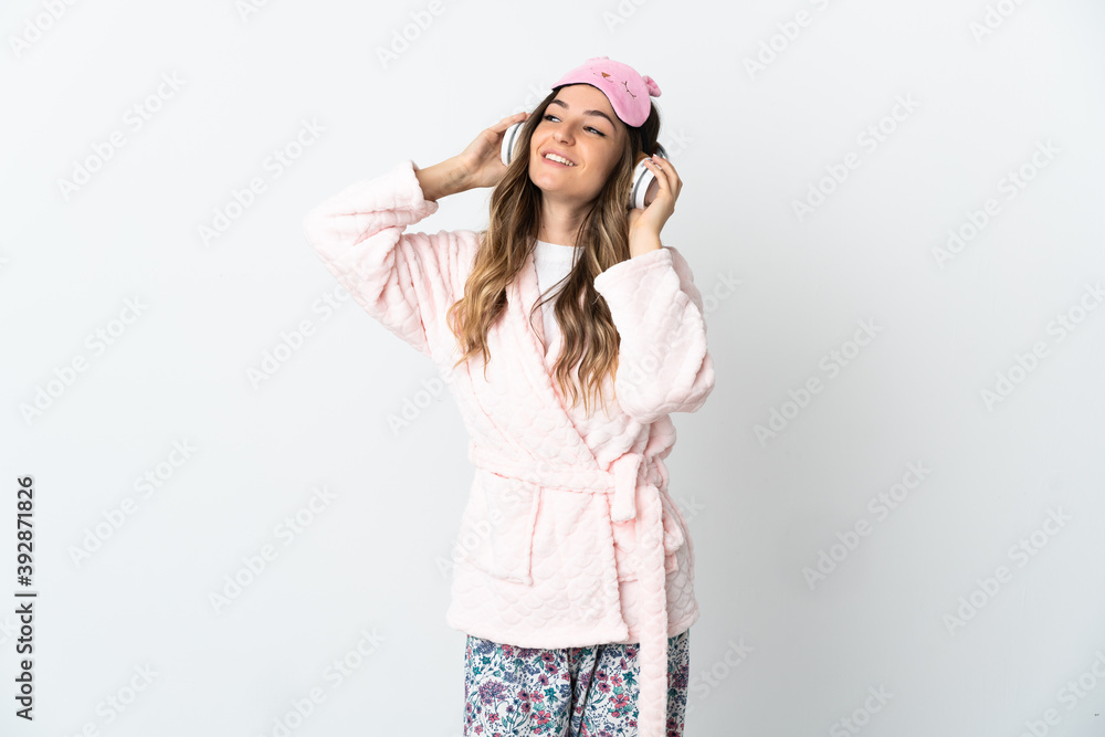 Young Romanian woman isolated on white background in pajamas and holding a pillow and listening music Young Romanian woman isolated on white background in pajamas and holding a pillow and listening music