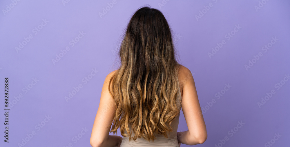 Fototapeta premium Young caucasian woman isolated on purple background in back position