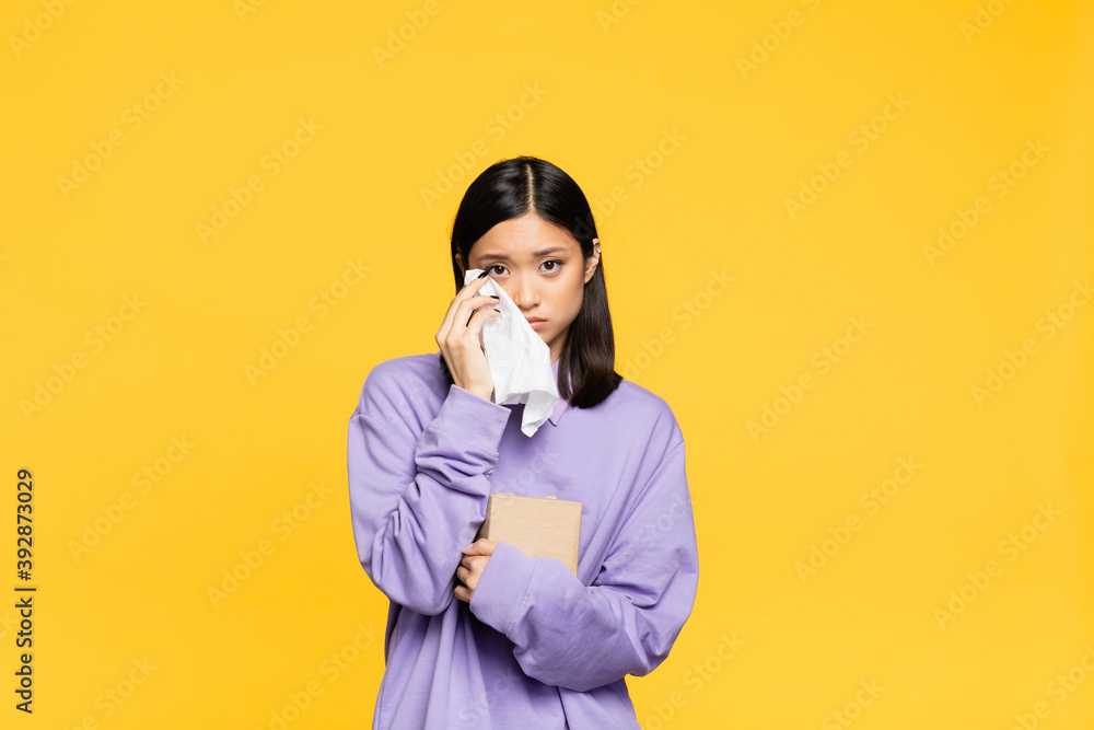 sad asian woman holding tissue box and napkin while crying isolated on yellow sad asian woman holding tissue box and napkin while crying isolated on yellow