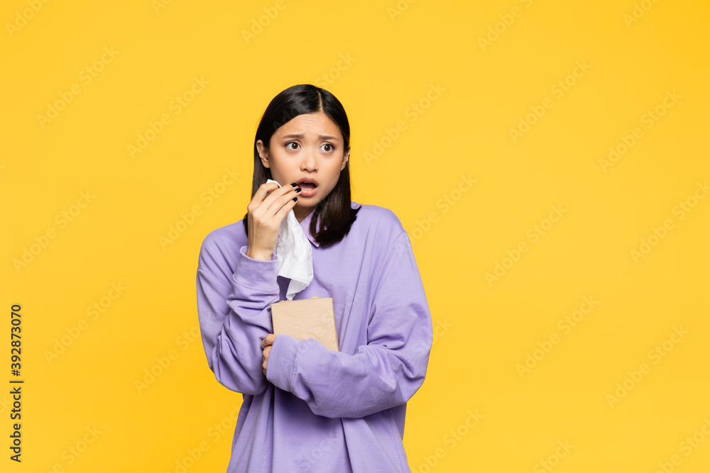 shocked asian woman holding tissue box and looking away isolated on yellow shocked asian woman holding tissue box and looking away isolated on yellow