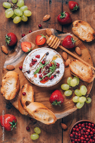 Baked camembert cheese with honey, rucola, cranberry, toasted bread, grape, strawberries, almond nuts on wooden board. Top view. Copy space. Romantic date night. Valentine's Day, love concept