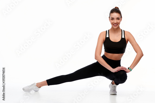 Fitness European girl doing stretching workout. Full length shot of young girl on white background. Stretching and motivation