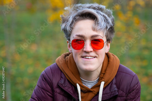 Young woman with stylish short hair, dressed in a gender neutral style. Style Element - Red Sunglasses. Close up portrait.