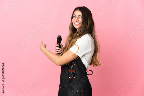 Young hairdresser woman isolated on pink background pointing back