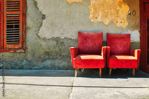 Quadro su tela Red Armchairs outside a house in disrepair