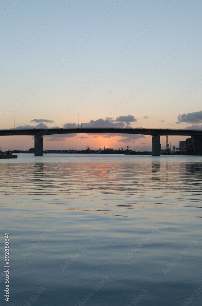 オレンジ色の夕焼けとシルエットの高架橋のある凪の港