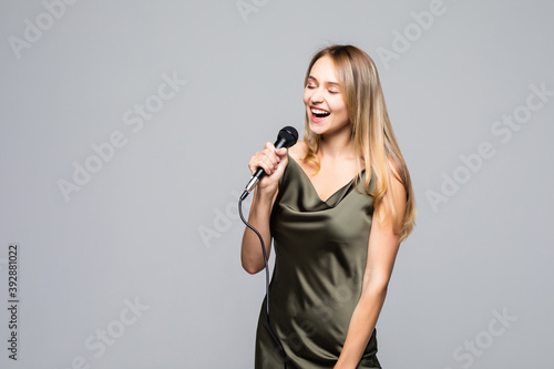 Beautiful young woman singing to microphone isolated on grey background