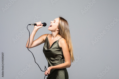 Beautiful young woman with microphone on grey background
