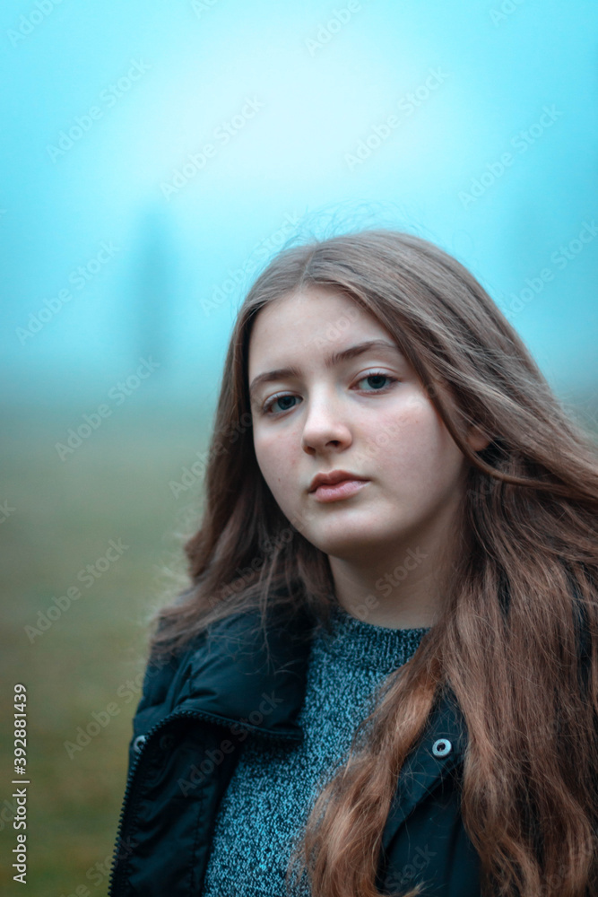 young woman with long blonde hair and black hut at foggy autumn day 