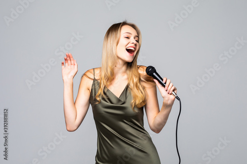Portrait of female singer wearing evening dress and keeping microphone on grey background. Concept of music photo