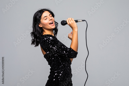 Beautiful brunette woman singing to microphone isolated on gray background photo