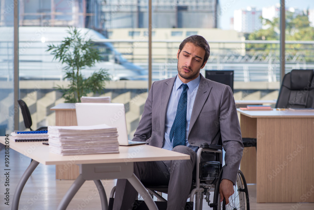 Young male employee in wheel-chair working in the office Young male employee in wheel-chair working in the office