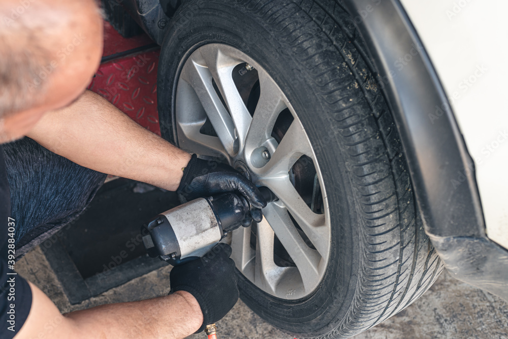 Car mechanic screwing or unscrewing car wheel of lifted automobile by pneumatic wrench at repair service station. Car mechanic screwing or unscrewing car wheel of lifted automobile by pneumatic wrench at repair service station.