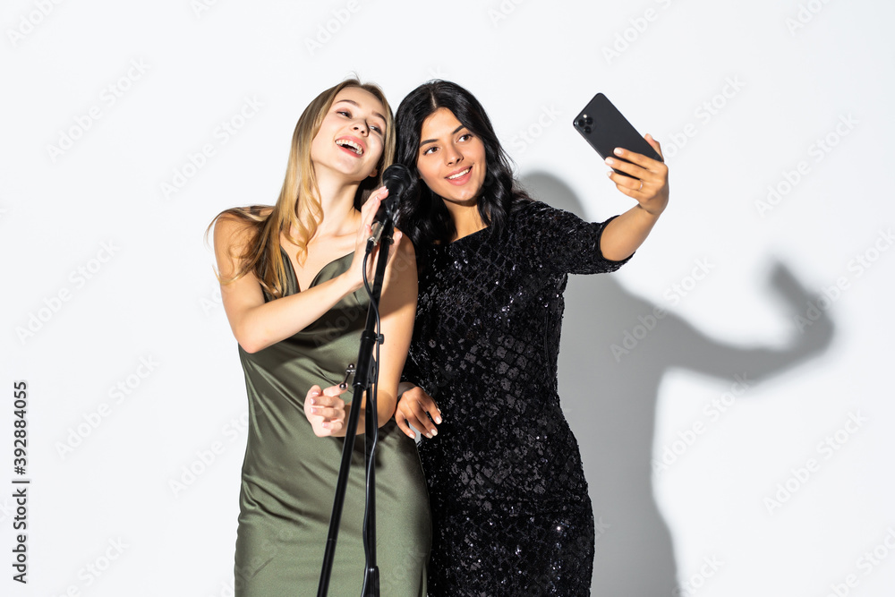 Two young women singing on karaoke and take selfie isolated on white background Two young women singing on karaoke and take selfie isolated on white background