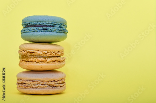 Fototapeta Naklejka Na Ścianę i Meble -  Multicolored macaroons in the form of a tower on a yellow background. Colorful greeting card with delicious almond cookies. Sponge cakes on top of each other. Spaces for text, copy space.